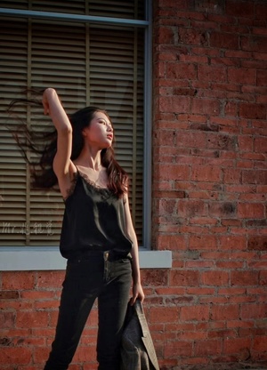 一位年轻女子站在街道上 面前有一座砖楼 她举起拳头在空中 窗外有窗户。