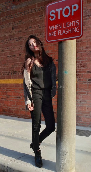 一名穿黑色衣服的年轻女子站在人行道上 旁边是一个柱子上的禁止停车标志。