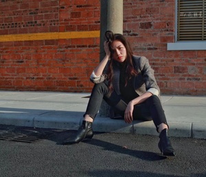 一个穿黑靴子的年轻女子坐在街边的路缘上。