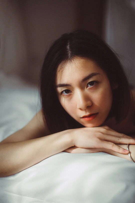 一个年轻女子躺在铺有白色床单的床上 手上戴着戒指 正对着相机。