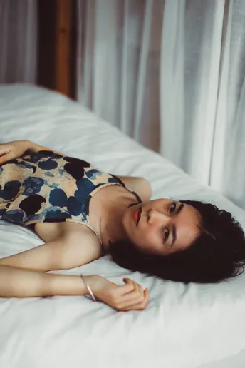 一个穿着连衣裙的年轻女子躺在铺有白色床单的床上