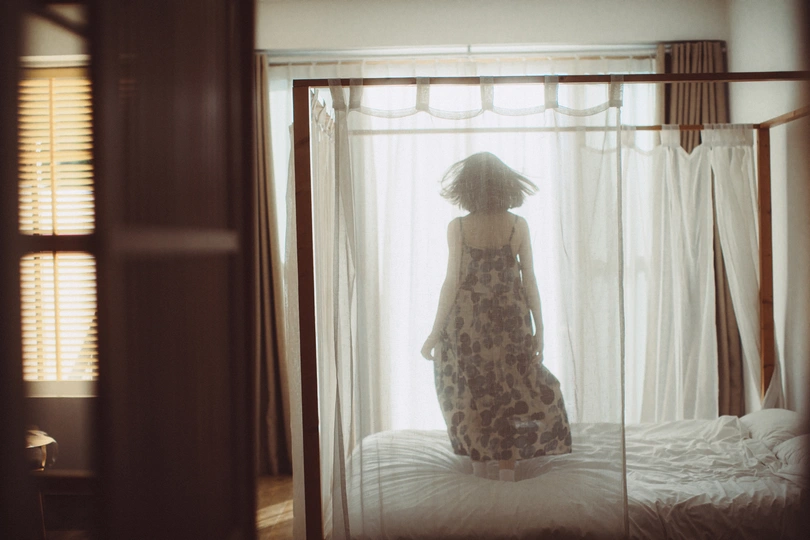 一位穿着连衣裙的女士站在卧室的打开窗户前