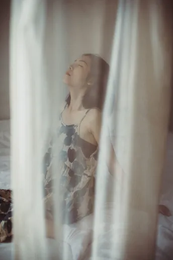 一个年轻女子坐在床上看窗户外。