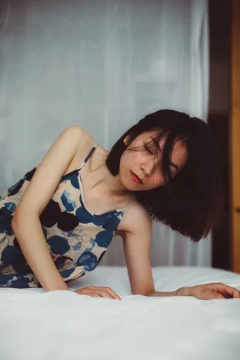 一个穿着连衣裙的年轻女子躺在铺有白色床单的床上