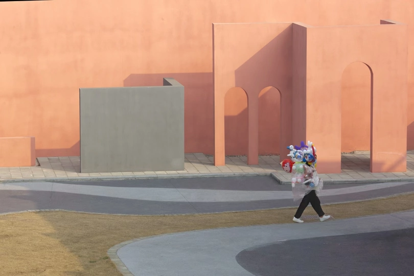 一位女士走在粉色墙壁的建筑物前的小巷中