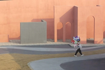 一位女士走在粉色墙壁的建筑物前的小巷中