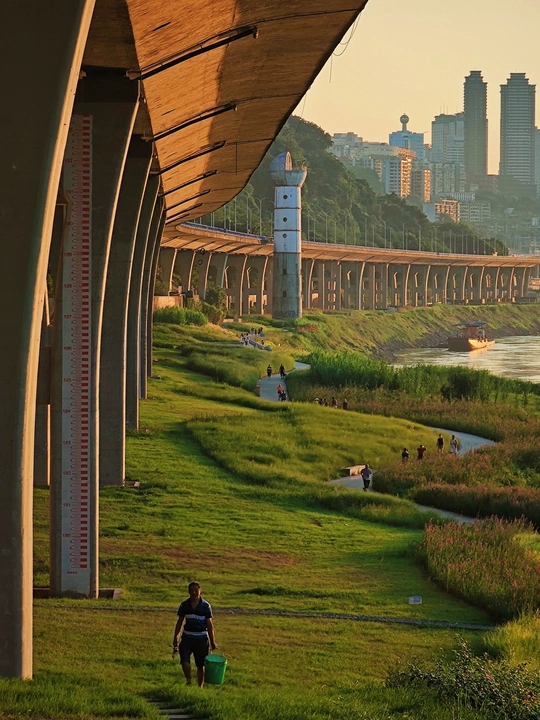 一个拿着水桶的男人走过一片绿草地 靠近一座桥和一片水域