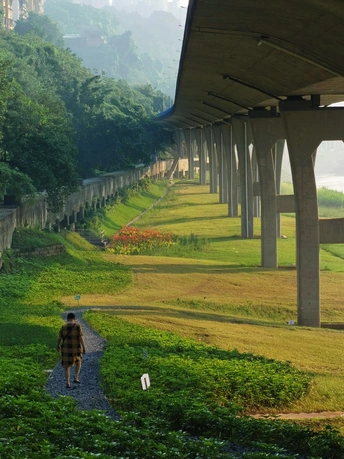 一个撑着雨伞的人在桥下的小路上行走