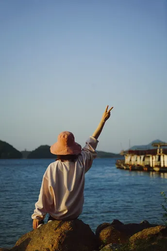 一位戴帽子坐在岩石上 双手指向水域的女子