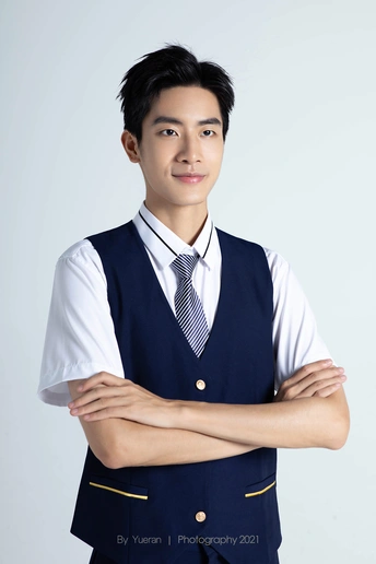 一位穿着蓝色背心和领带的年轻人交叉着双臂 为肖像摆姿势。