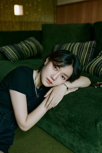 一个年轻女子坐在绿色沙发上 在一个深绿色房间里 为相机摆姿势。