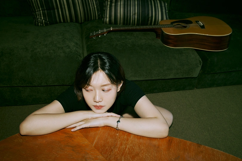 一个年轻女子躺在地上 双手放在桌子上 一把吉他靠在她身后。