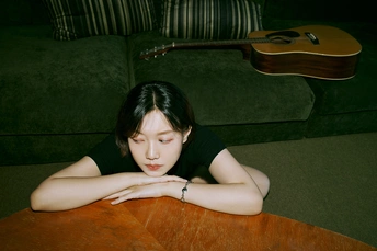一个年轻女子躺在地上 双手放在桌子上 一把吉他靠在她身后。