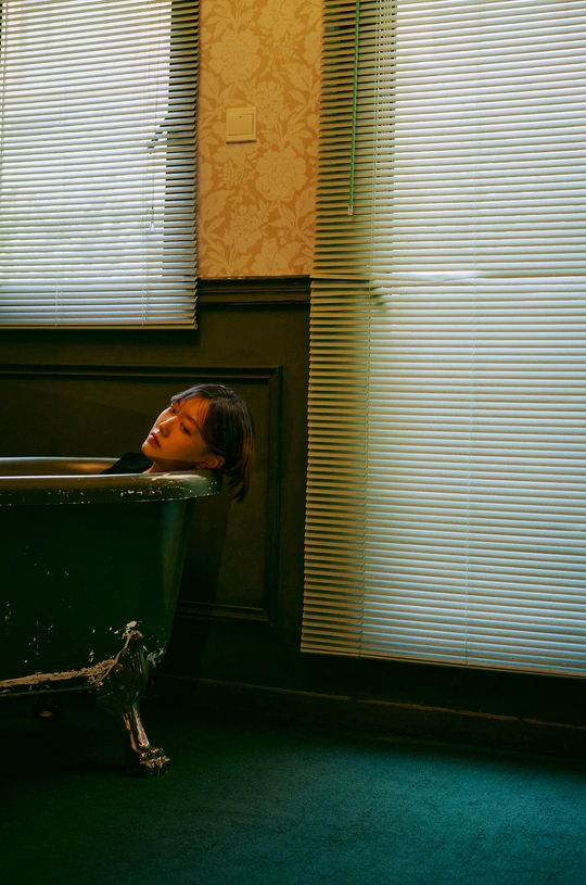 一个年轻女孩坐在浴缸里 浴室里有窗帘 窗户上没有窗帘。