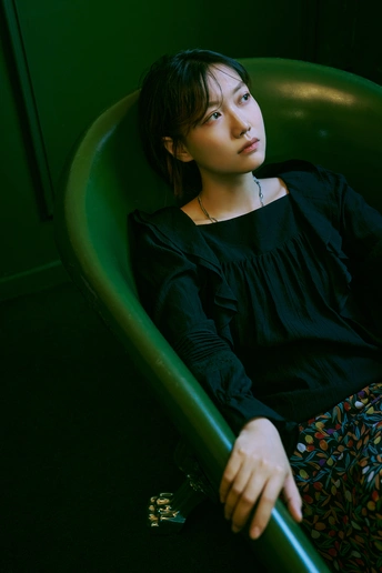 一个年轻女子坐在一个绿椅上 在一个光线昏暗的房间里。