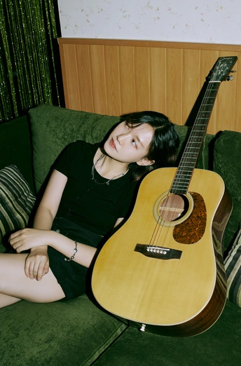 一个年轻女子坐在一把绿色沙发旁 旁边有一把吉他。
