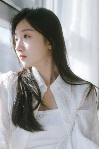 一位年轻女子穿着白色衬衫 正在看窗户外面的景色。