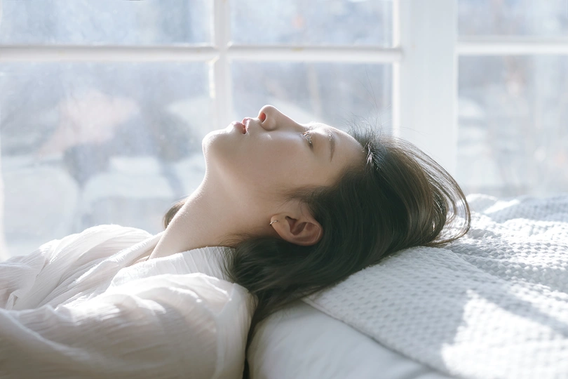 一个年轻女子躺在白色床上 她的头靠在窗户上