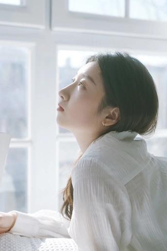 一个年轻女子坐在床上 正在看窗外的书。