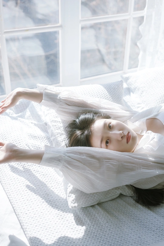 一个穿着白色连衣裙的年轻女子躺在铺有白色床单的床上