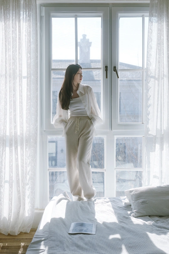 一个年轻女子站在床上 朝窗外看。