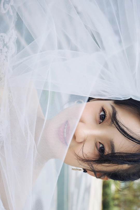 一位年轻女子透过带有白色窗帘的窗户凝视着相机