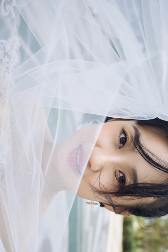 一位年轻女子透过带有白色窗帘的窗户凝视着相机