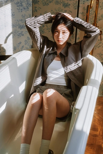 一个穿着西装的年轻女子坐在一个白色的椅子上 身后有一个浴缸。