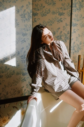 一个穿着白衬衫的年轻女子坐在一个有花卉图案的白色床上。