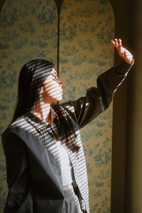 一个年轻女子站在一扇窗户透出的阳光照亮的房间里