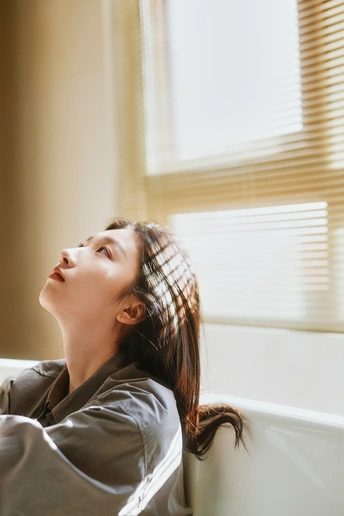 一个年轻女子坐在浴缸里 在一个浴室里 透过窗户看着天空。