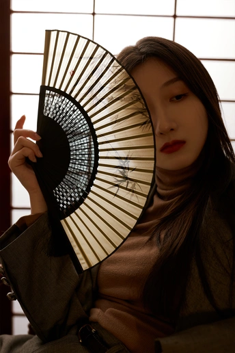 一位年轻女子举着扇子挡在面前 站在窗户前摆姿势