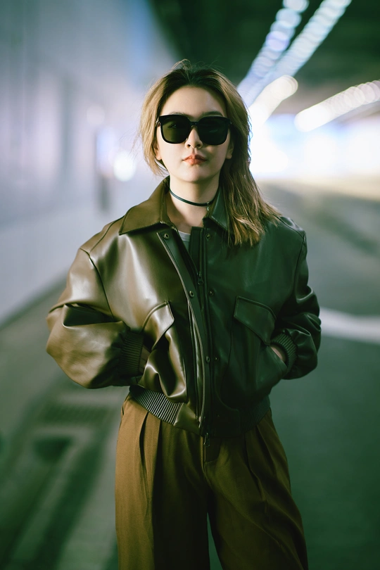 一个戴太阳镜和黑色夹克站在地铁隧道里的年轻女子