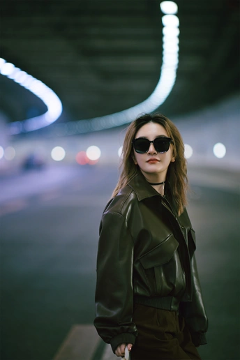 一个戴太阳镜和黑色皮夹克的女青年站在地铁隧道里夜间