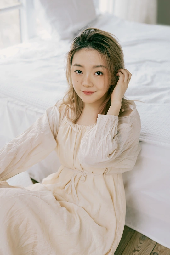 一个穿着白衬衫的年轻女子坐在床前地板上 为相机摆姿势。