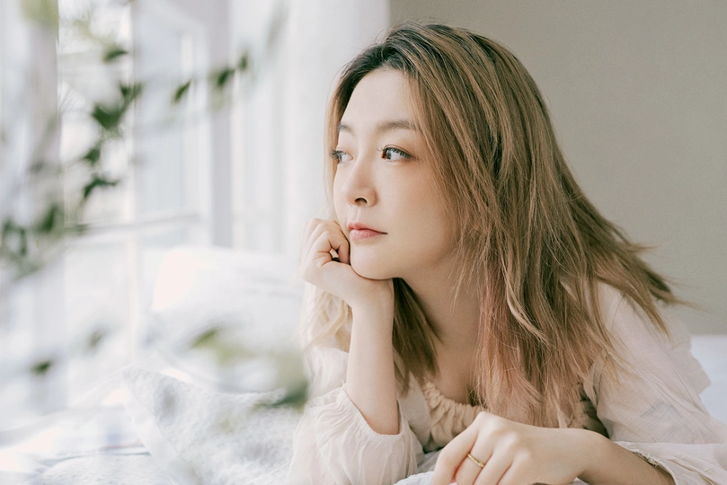 一位年轻美丽的女子坐在白色床上 凝视着窗外。