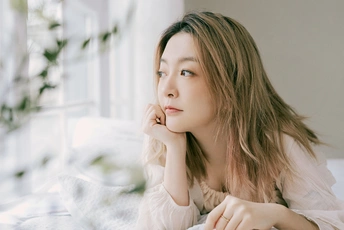 一位年轻美丽的女子坐在白色床上 凝视着窗外。