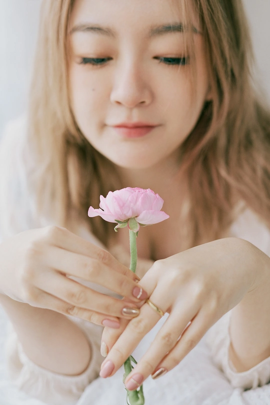 一个戴戒指的年轻女子手里拿着一朵粉色花。