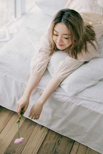 一个年轻女子躺在白色床上 手里拿着一束花。