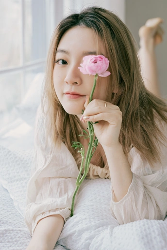 一位年轻女子坐在床上 手里拿着一朵粉红色玫瑰。