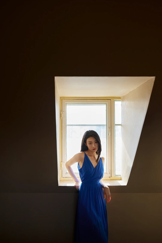 一位穿着蓝色连衣裙站在光线昏暗的房间里的女人