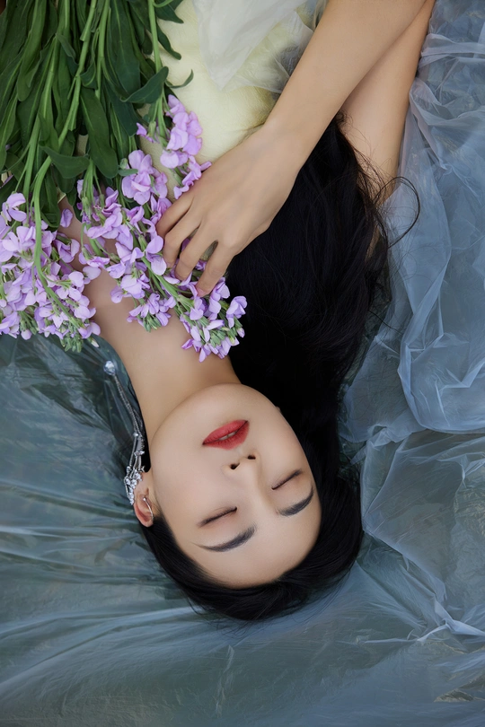 一个穿着美丽裙子的年轻女子躺在水中 头上飘着紫色的花朵。