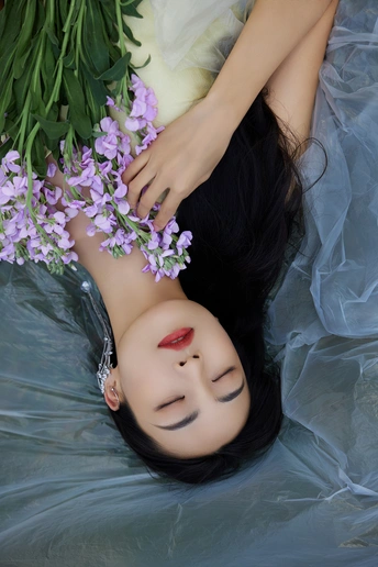 一个穿着美丽裙子的年轻女子躺在水中 头上飘着紫色的花朵。