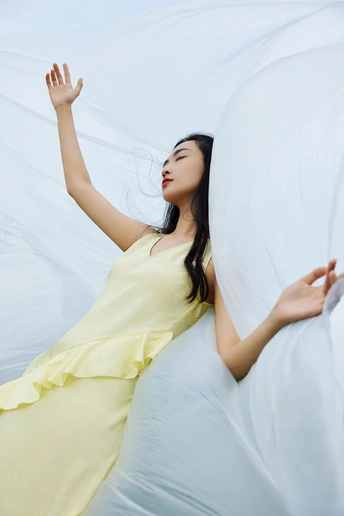 一位美丽的年轻女子穿着黄色裙子在天空中飘浮 双手举过头顶。