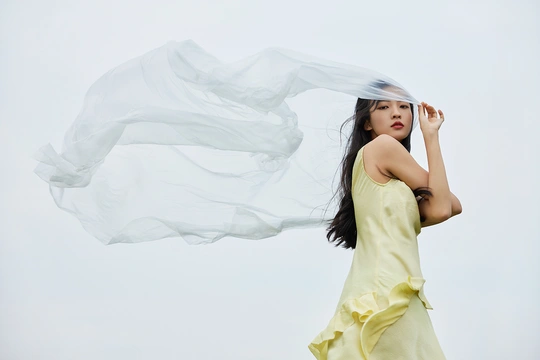 一位穿着黄色连衣裙 手持白色雨伞站在风中的年轻女子