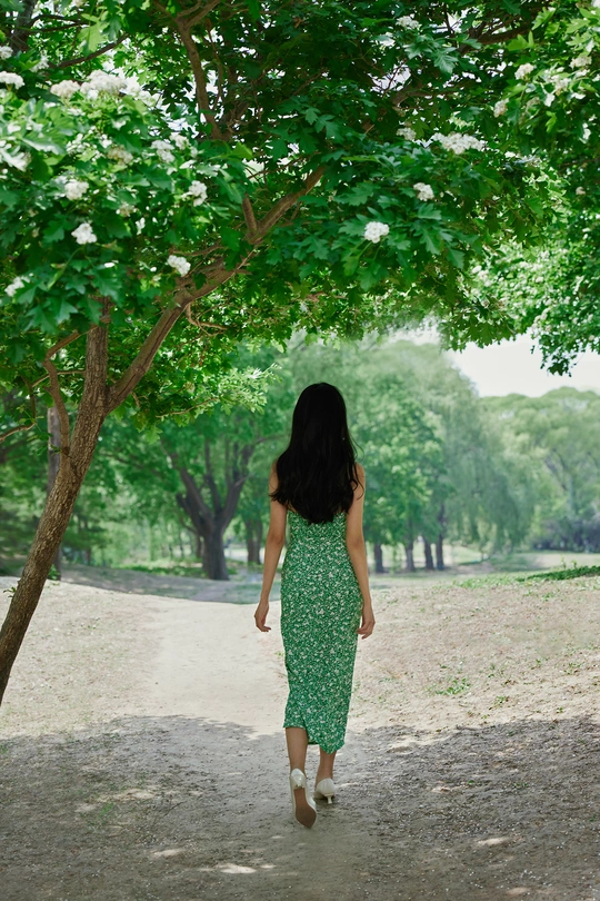 一位穿着绿色连衣裙的年轻女子走在树木下的小径上
