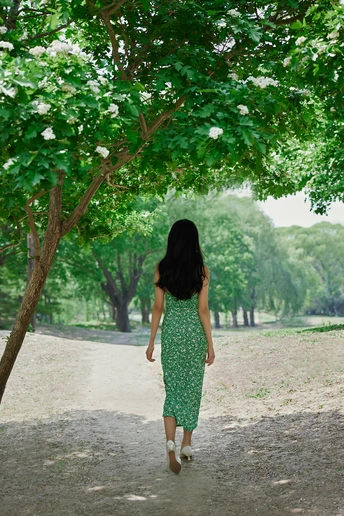 一位穿着绿色连衣裙的年轻女子走在树木下的小径上