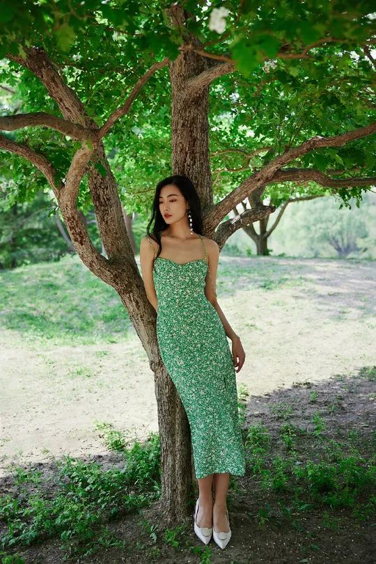 一位穿着绿裙子的年轻女子站在一棵树下
