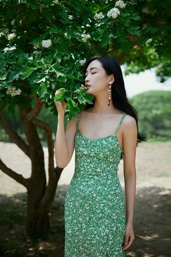 一位穿着绿裙子的美丽年轻女子站在一棵树下