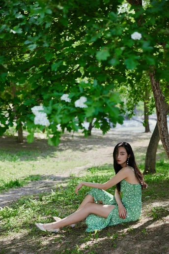 一位穿着绿色连衣裙的年轻女子坐在公园中的一棵树的阴影下